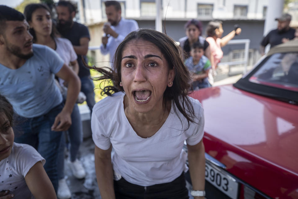 A Syrian woman screams for help for her husband who was injured by stone throwing by members of the Lebanese Forces group, who attacked buses carrying Syrians traveling to vote in the town of Zouk Mosbeh, north of Beirut, Lebanon, Thursday, May 20, 2021. Mobs of angry Lebanese men attacked vehicles carrying Syrians expatriates and those who fled the war heading to the Syrian embassy in Beirut on Thursday, protesting against what they said was an organized vote for President Bashar Assad. (AP Photo/Hassan Ammar)