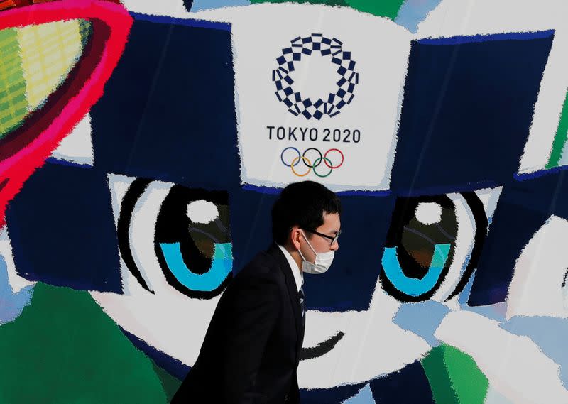 FILE PHOTO: A man wearing a protective mask walks past a large poster featuring Tokyo 2020 Olympic Games mascot Miraitowa amid the coronavirus disease (COVID-19) outbreak in Tokyo