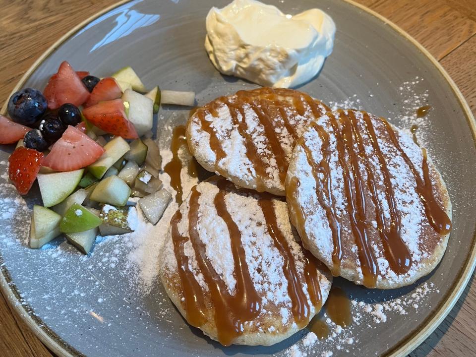 Pancakes with caramel and powdered sugar on a plate with fruit