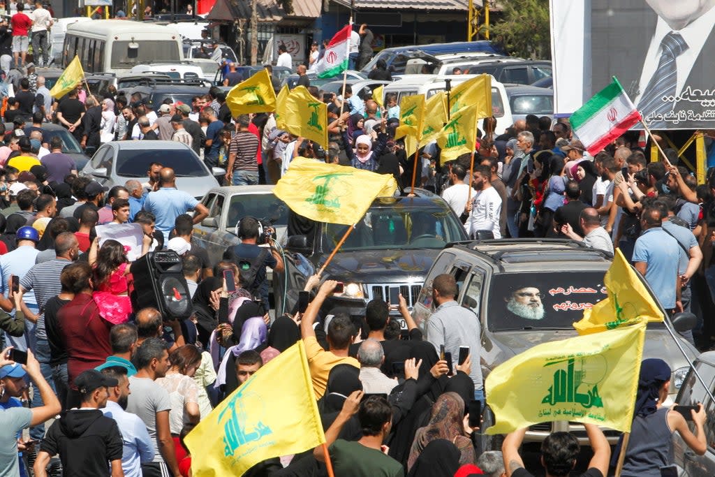 People wave Hezbollah and Iranian flags as a convoy of tanker trucks carrying Iranian fuel drives through the streets  (REUTERS)