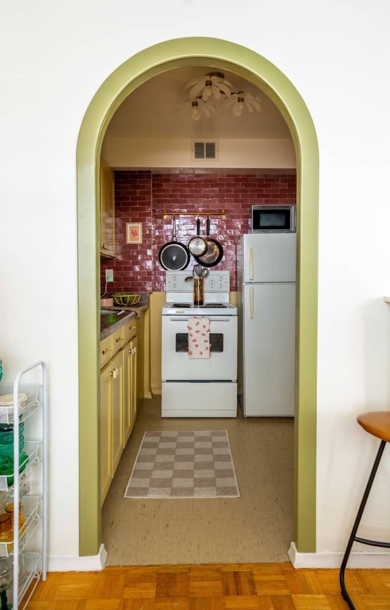 View looking into kitchen with yellow painted cabinets, a red tile backsplash, and dark brown speckled countertops