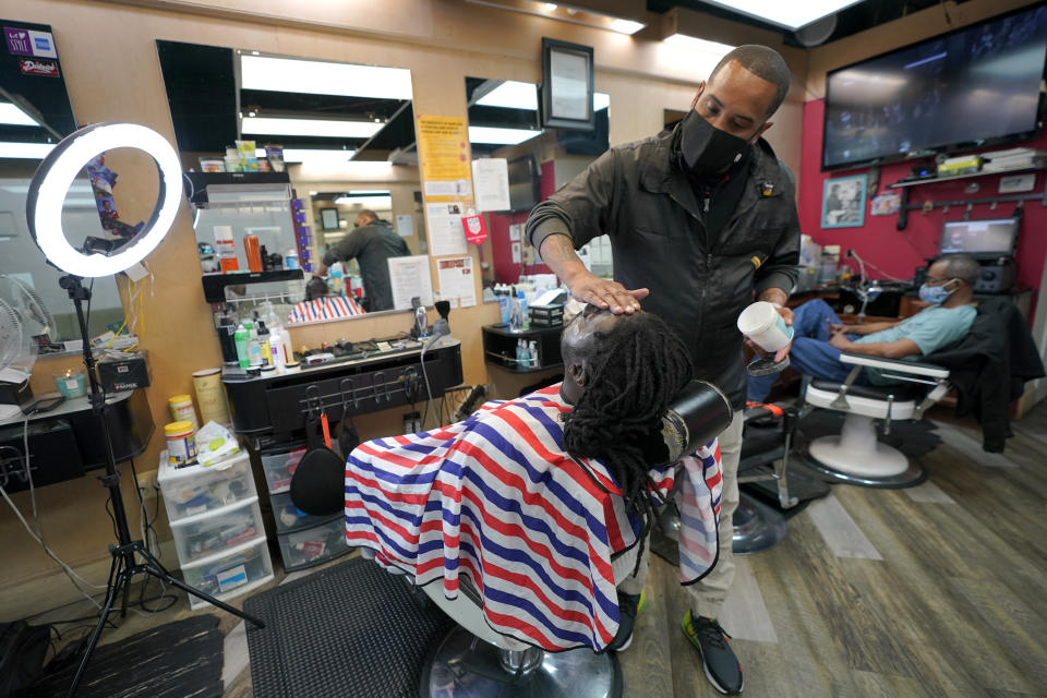 Mike Brown, right, a barber and health advocate, lines up the facial hair of Vyron Cox Jr., Friday, April 9, 2021, in Hyattsville, Md. Brown is a member of the Health Advocates In Reach & Research (HAIR) program, which helps barbers and hair stylists to get certified to talk to community members about health. During the COVID-19 pandemic, Brown and a team of certified barbers have been providing factual information to customers about vaccines, a topic that historically has not been trusted by members of black communities because of the health abuse the race has endured over the years. (AP Photo/Julio Cortez)