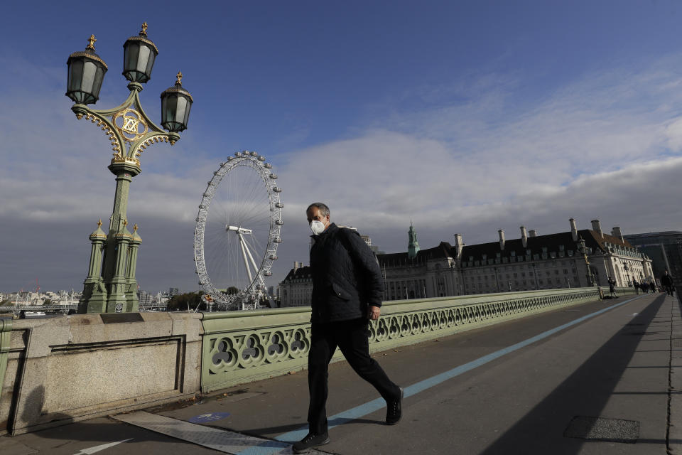 A man wearing a face mask walks past the London Eye on Westminster Bridge in London, Friday, Oct. 16, 2020. The British government is sticking to its strategy of tiered, regional restrictions to combat COVID-19 amid mounting political and scientific pressure for stronger nationwide measures to prevent the pandemic from spiraling out of control. (AP Photo/Kirsty Wigglesworth)