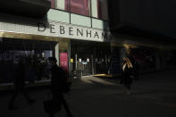 People wearing face masks walk past the Debenhams flagship department store on Oxford Street, in London, Tuesday, Dec. 1, 2020. In another dark day for the British retailing industry, Debenhams said Tuesday it will start liquidating its business after a potential buyer of the company pulled out, a move that looks like it will cost 12,000 workers their jobs. (AP Photo/Matt Dunham)