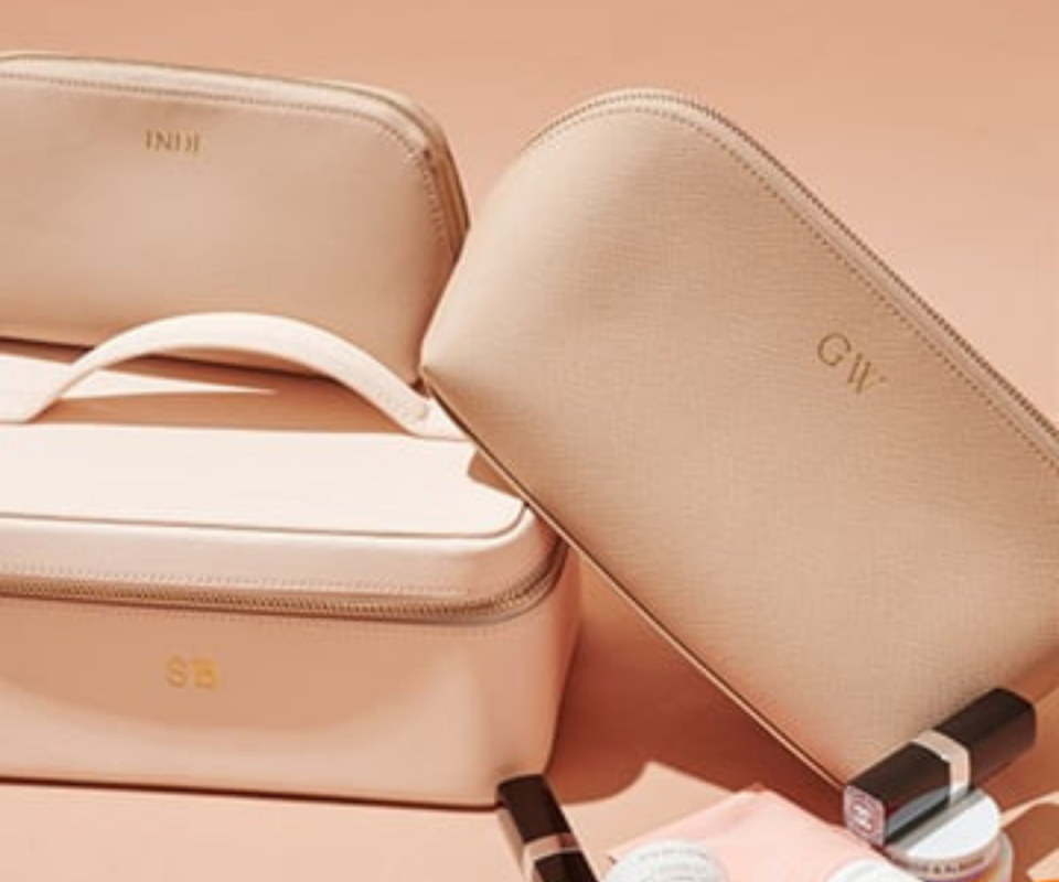 A collection of peach coloured makeup bags and leather zip jewellery bags sitting on top of each other infront of a peach background