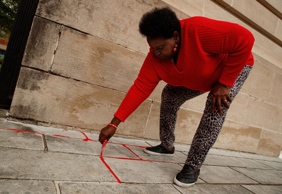 Birdie Hardison, a resident of Columbia, pours red sand into the cracks outside of the Maury County courthouse during a Red Sand Project event hosted by her daughter, Jennifer Kinzer Parks, in Columbia, Tenn. on Apr. 27, 2023. 