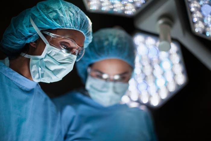 Two surgeons in surgical scrubs, masks, and caps working under bright operating room lights