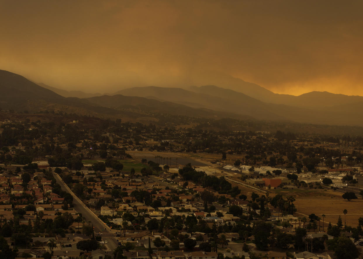 An aerial view of a mix of rain and smoke over a hillside.