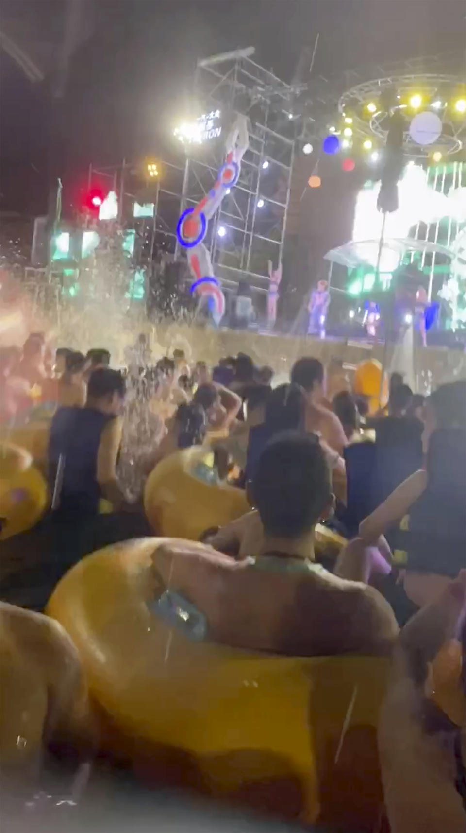 This image made from an Aug 3, 2020 video shows crowd gather in a pool as they watch performers on a stage at Wuhan Maya Beach Water Park in Wuhan, central China. For more than two months, the 11 million residents of Wuhan endured a strict lockdown as coronavirus raced around the city. Now, some are letting loose en masse at rocking nighttime pool parties at the popular amusement park chain. The park reopened in late June, and the crowds have picked up in August. (anonymous photo via AP)