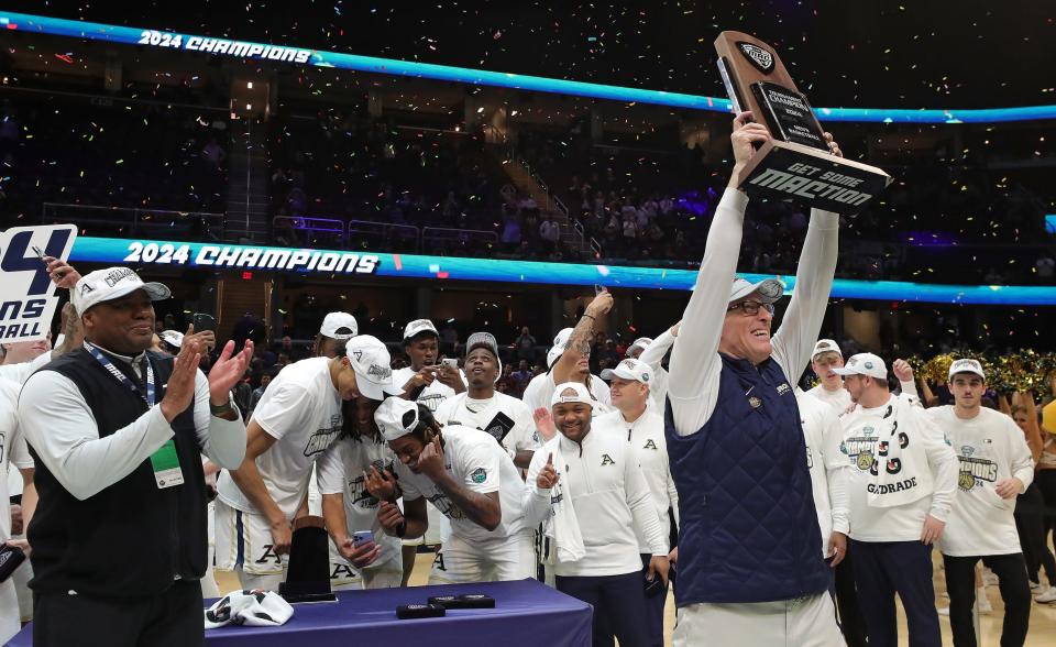 Akron coach John Groce proudly shows off the MAC Championship trophy after the Zips defeated Kent State in the Mid-American Conference Tournament championship game Saturday in Cleveland.