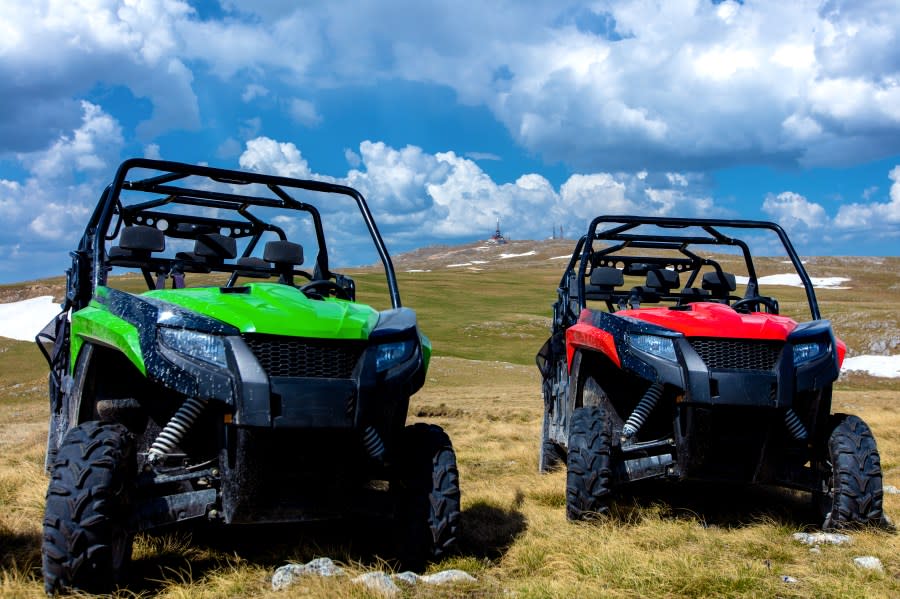 Parked UTV, buggies on mountain peak with clouds and blue sky in background.