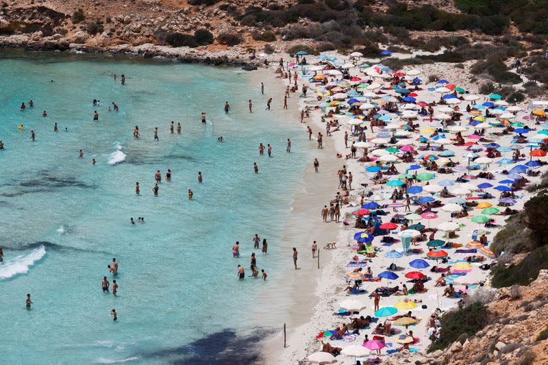 FILE PHOTO: People sunbathe on the beach on the Sicilian island of Lampedusa, as a flow of migrants arriving on the Mediterranean island, in Lampedusa, Italy, June 22, 2021.