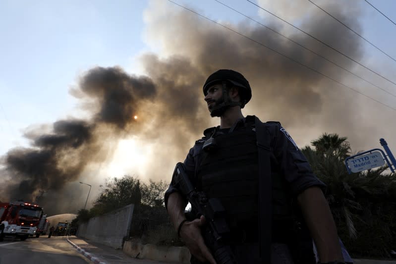 An Israeli security forces personnel stands guard as firefighters work to extinguish a fire in a factory in Sderot, southern Israel