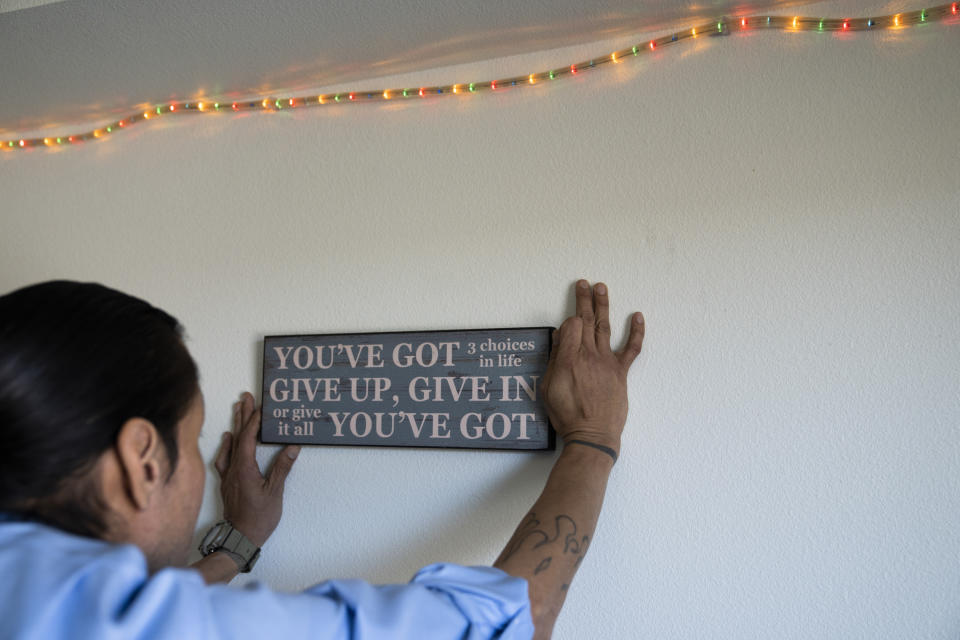 Cheyenne Welbourne adjusts a sign in his apartment at The Starlight affordable housing building that is run by Central City Concern, a Portland-based homeless services nonprofit, on Friday, March 15, 2024, in Portland, Ore. Welbourne moved into one of the nonprofit's single room occupancy units in downtown Portland last March after years of living on the streets. (AP Photo/Jenny Kane)