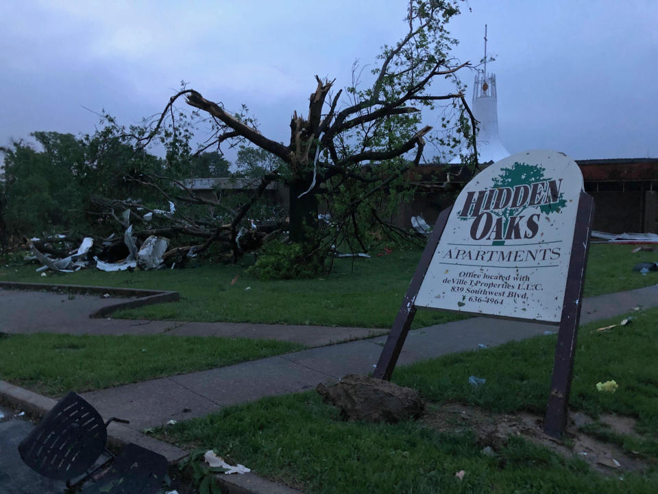 The sign for the Hidden Oaks apartment complex in Jefferson City Missouri stands bent Thursday, May 23, 2019, from a tornado in front of a tree that was ripped apart. The National Weather Service has confirmed a large and destructive tornado has touched down in Missouri's state capital, causing heavy damage and trapping multiple people in the wreckage of their homes. (AP Photo/David A. Lieb)