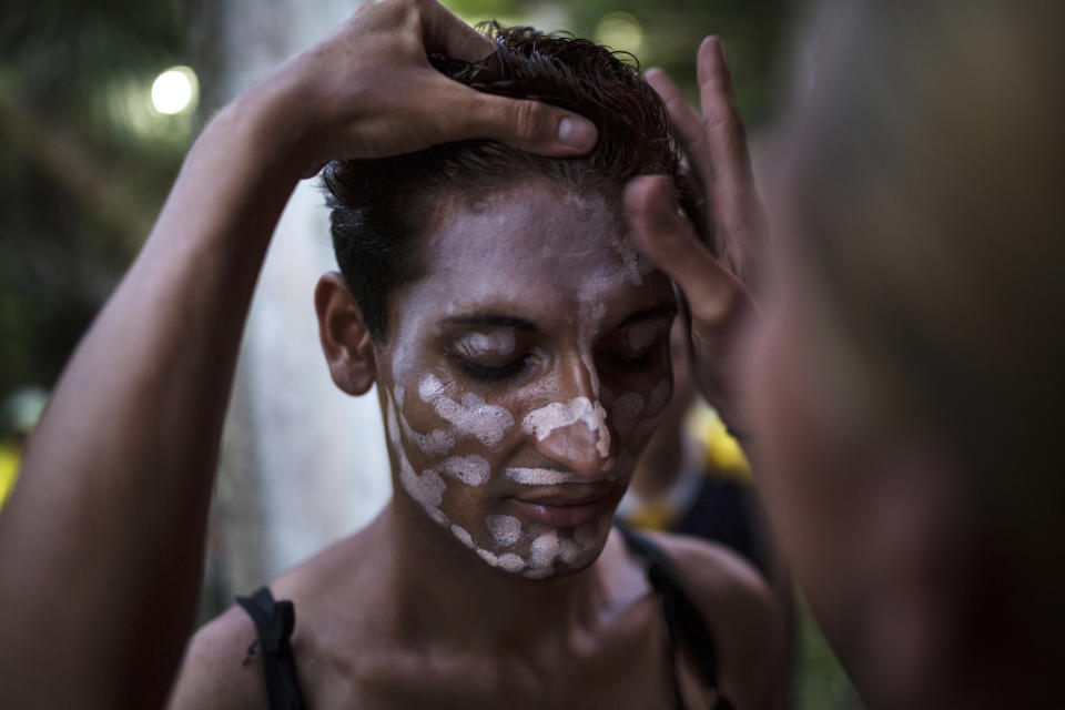In this Nov. 1, 2018 photo, Honduran transgender Junior Castro, 22, who is part of the Central American migrants caravan hoping to reach the U.S. border, stands still as a friend applies foundation to her face, in Donaji, Mexico. Sticking out among the crowd for their bright clothing and makeup, the group has suffered verbal harassment, especially from men. (AP Photo/Rodrigo Abd)