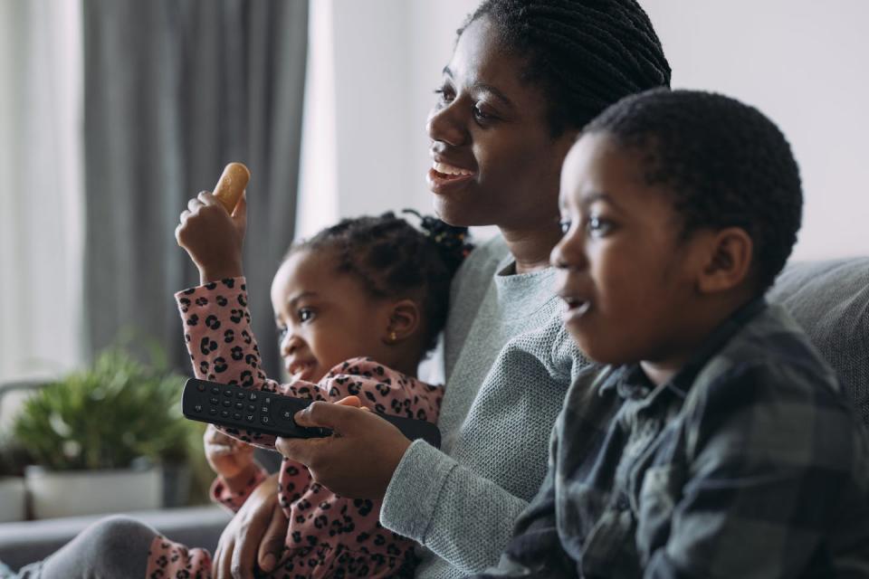 Smiling parent sitting with two children watching TV together