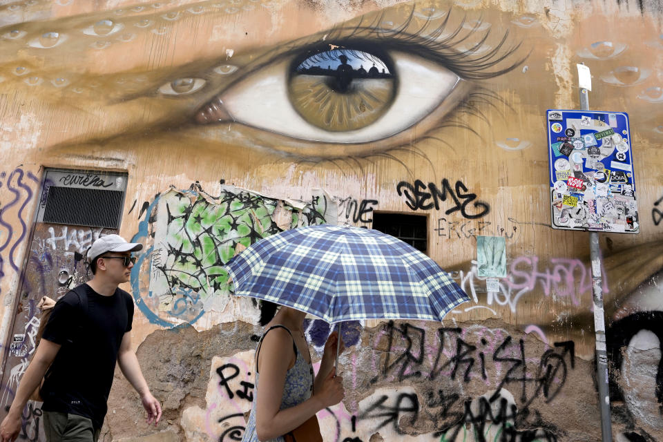 A woman uses an umbrella to take shelter from the sun as she walks in downtown Rome, Thursday, July 13, 2023. An intense heat wave has reached Italy, bringing temperatures close to 40 degrees Celsius in many cities across the country.(AP Photo/Alessandra Tarantino)