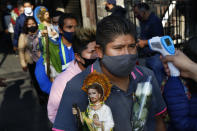 Un devoto con una mascarilla protectora para protegerse del nuevo coronavirus, permite que le tomen la temperatura antes de ingresar a la iglesia católica San Hipólito como parte de la peregrinación anual en honor a San Judas, el santo patrón de las causas perdidas, en la Ciudad de México, el miércoles 28 de octubre de 2020. (AP Foto/Marco Ugarte)