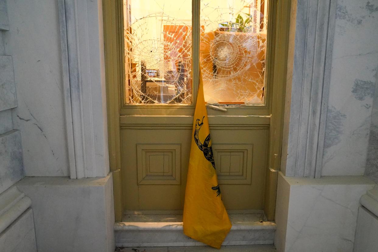 A flag hangs between broken windows after President Donald Trump supporters tried to break through police barriers outside the U.S. Capitol, Wednesday, Jan 6, 2021.