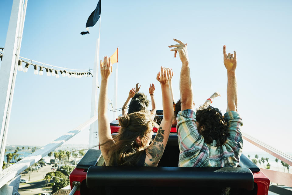 Rear view of couple with arms raised about to begin descent on roller coaster in amusement park