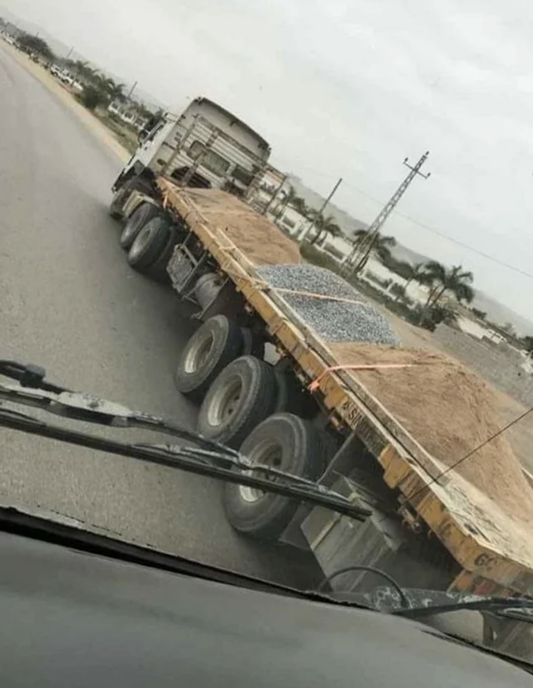 A 18-wheeler is transporting sand and gravel, but the only things holding them in place are cords pulled over the top, with nothing holding them in on the sides