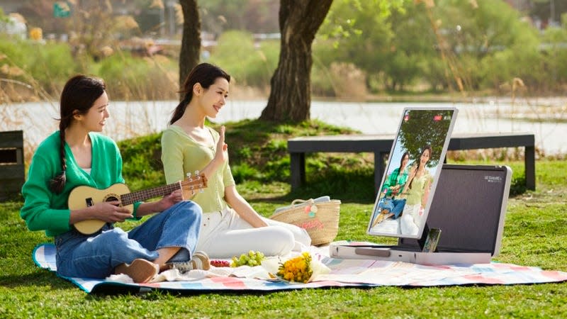 Two people in a park having a picnic using the new LG StanbyME to stream themselves playing music.