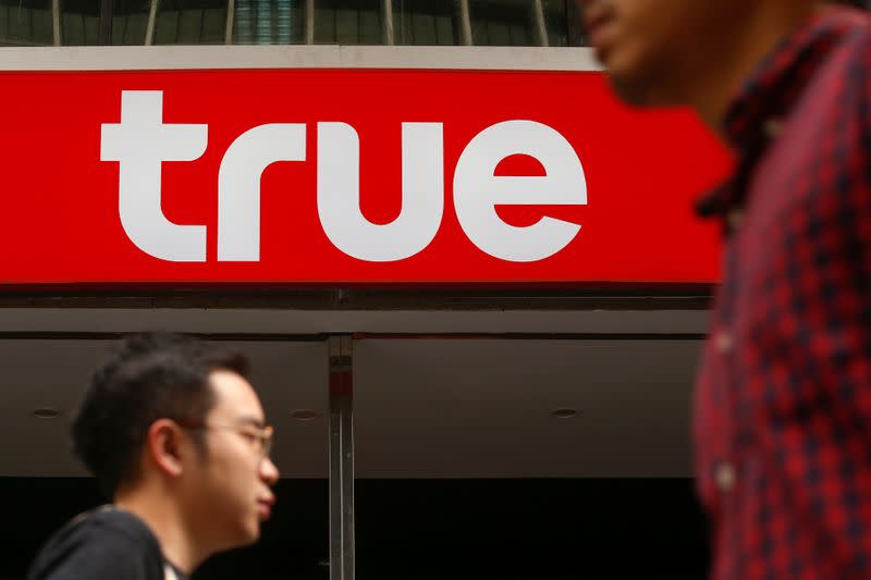 People walk past the logo of True Corp in Bangkok