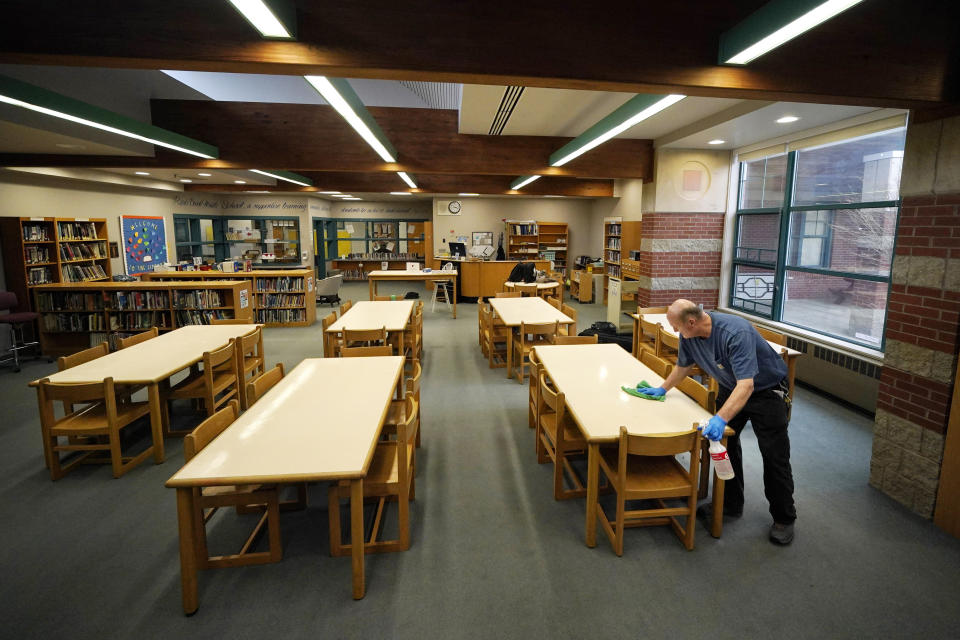 Custodian David Bishop cleans pencil marks from desks in the Hampden Academy library, Tuesday, April 25, 2023, in Hampden, Maine. In addition to his custodial duties, Bishop also serves as the chess coach for district's nationally recognized middle school chess team. (AP Photo/Robert F. Bukaty)