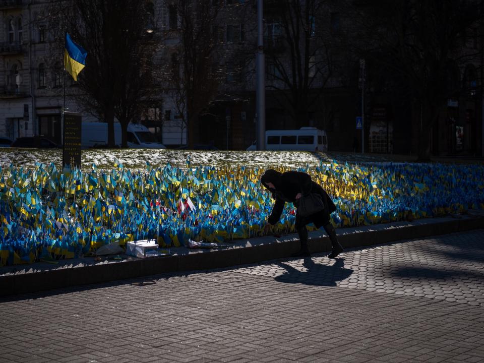 A woman places a Ukrainian flag at a memorial for those killed during the war, near Maidan Square in central Kyiv (AP)