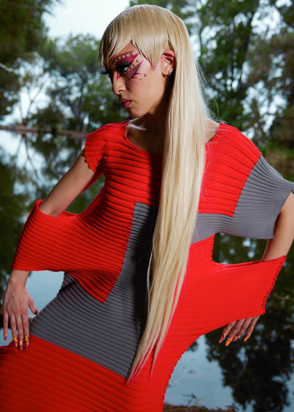 A model with long blond hair in a red ribbed dress decorated with dark geometric shapes