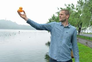 L’artiste néerlandais Florentijn Hofman, tenant un “Rubber Duck” miniature sur les berges d’un lac à Hangzhou (Chine), en juin 2013.. Photo Shan He/Imaginechina/AFP