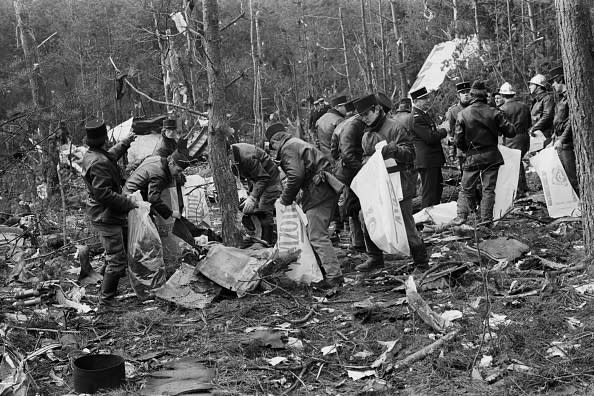 Group of individuals in a wooded area collecting debris and pieces of material from the ground