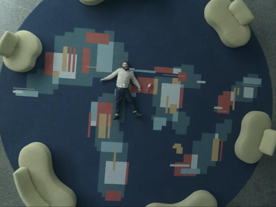 clark in station eleven laying on a carpet that shows representations of the great lakes, drawn out in blocky shapes, on a blue background