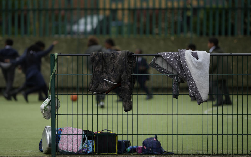 Children's coats hang off a fence as they play soccer during their lunch break at the Holy Family Catholic Primary School in Greenwich, London, Thursday, May 20, 2021. (AP Photo/Alastair Grant)