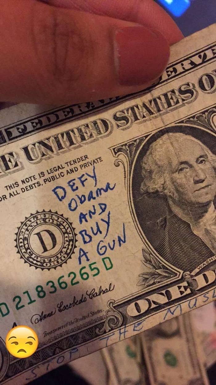 A hand holding a U.S. dollar bill with handwritten text saying, "Defy Obama and buy a gun." There is a face with a disappointed expression at the bottom left