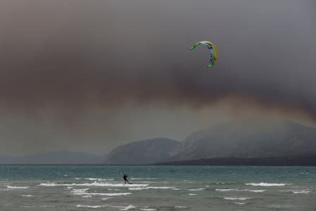 A man kitesurfs near the shores of the city of Chalkida as smoke rises from a wildfire burning on the island of Evia