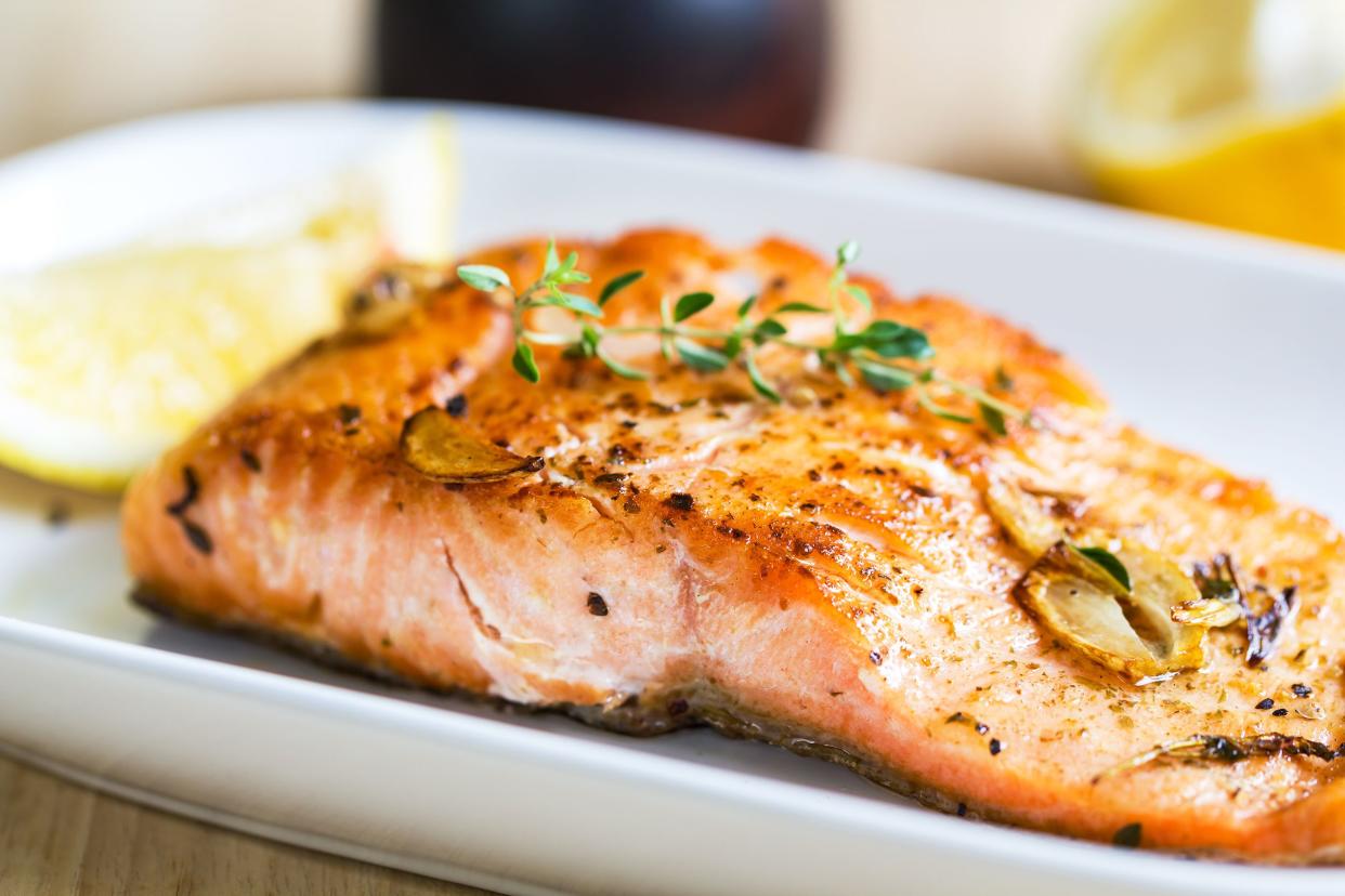 A filet of cooked salmon on a white porcelain plate, selective focus, with a lemon, on a table, with a blurred background