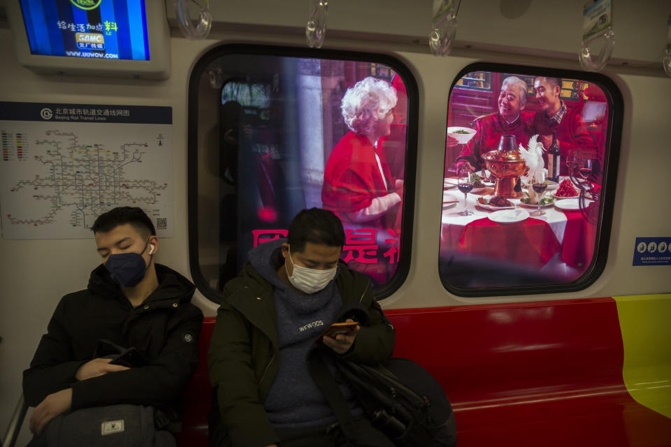 People wear masks on a subway train as it stops near a billboard showing a family having a New Year's banquet meal in Beijing, Friday, Jan. 24, 2020. A virus that has killed more than two dozen people and sickened hundreds more has all but shut down China's biggest holiday of the year, the Lunar New Year. Instead of family reunions or sightseeing trips, many of the country's 1.4-billion people are hunkering down as the country scrambles to prevent the illness from spreading further. (AP Photo/Mark Schiefelbein)