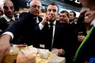 French President Emmanuel Macron eats cheese during a visit to the 57th International Agriculture Fair (Salon international de l'Agriculture) at the Porte de Versailles exhibition center in Paris