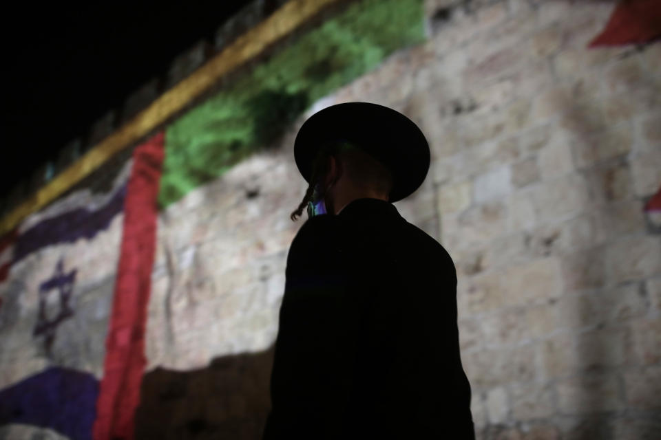 An ultra-Orthodox Jewish man walks past representations of the Israeli, Emirati and Bahraini flags projected onto a wall of Jerusalem's Old City, marking the day of a signing ceremony in Washington signifying the two Gulf nations' normalization of relations with Israel, Tuesday, Sept. 15, 2020. (AP Photo/Maya Alleruzzo)