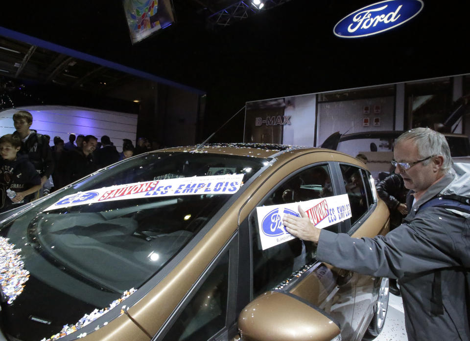 A protestor from a Ford factory in France attaches a giant sticker that reads: "Save the Jobs" to a car during a protest against factory policy at the Paris Auto Show, France, Saturday, Sept. 29, 2012. The workers swarmed the Paris Auto Show with giant stickers, plastering about 20 cars around the hall to protest lost jobs in the automotive industry. (AP Photo/Michel Euler)