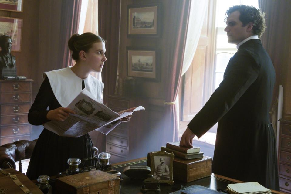 Millie Bobby Brown holds a newspaper while talking to Henry Cavill in 'Enola Holmes.'