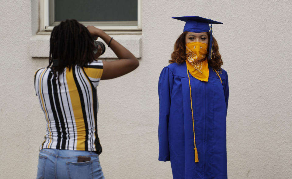 Anderson High School senior Teyaja Jones, right, poses in her cap and gown and a bandana face cover, Tuesday, May 5, 2020, in Austin, Texas. Texas' stay-at-home orders due to the COVID-19 pandemic have expired and Texas Gov. Greg Abbott has eased restrictions on many businesses that have now opened, but school buildings remain closed. (AP Photo/Eric Gay)