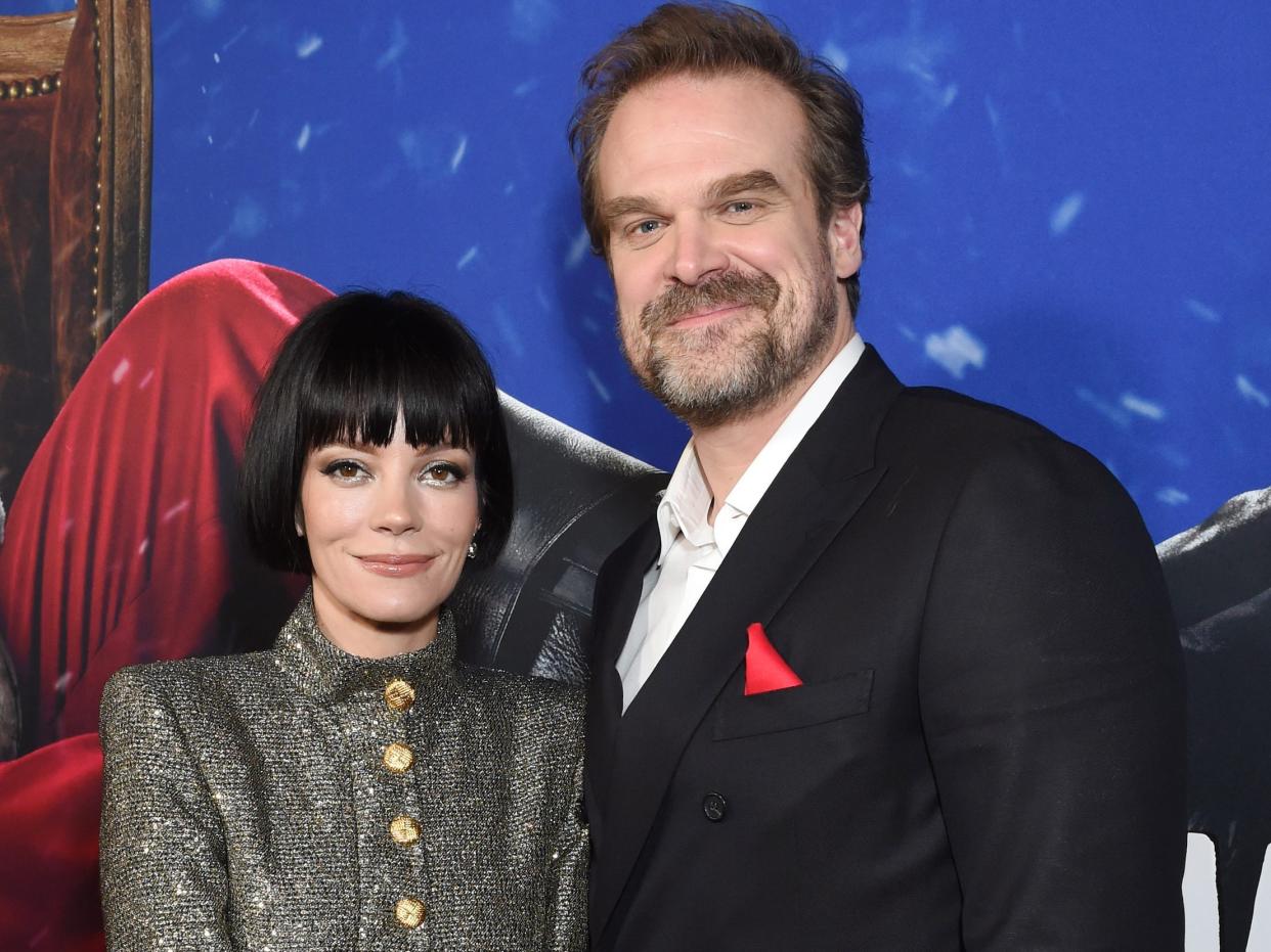 Lily Allen, in a gray sparkly suit, poses on the red carpet with husband David Harbour, in a black suit with red pocket square.