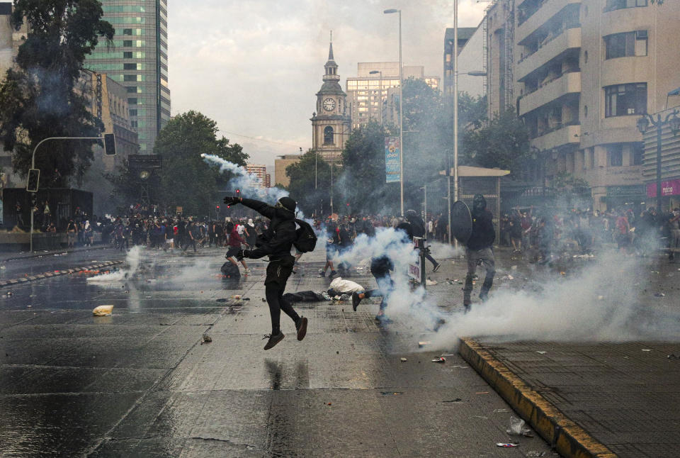 Anti-government protester returns a tear gas canister launched by Chilean police during a protest march in Santiago, Chile, Friday, Oct. 25, 2019. A new round of clashes broke out Friday as demonstrators returned to the streets, dissatisfied with economic concessions announced by the government in a bid to curb a week of deadly violence.(AP Photo/Esteban Felix)