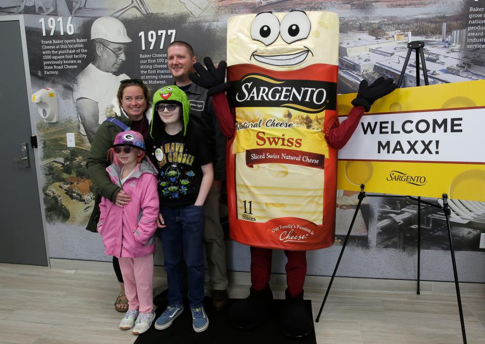 The Ball family of Winston-Salem, North Carolina, poses with the Sargento mascot before getting a tour on how string cheese is produced at the plant, Tuesday, November 22, 2022, in St. Cloud, Wis. Through Make-A-Wish, Maxx Bell, 10, with green hat, was given a chance to see how string cheese is produced.