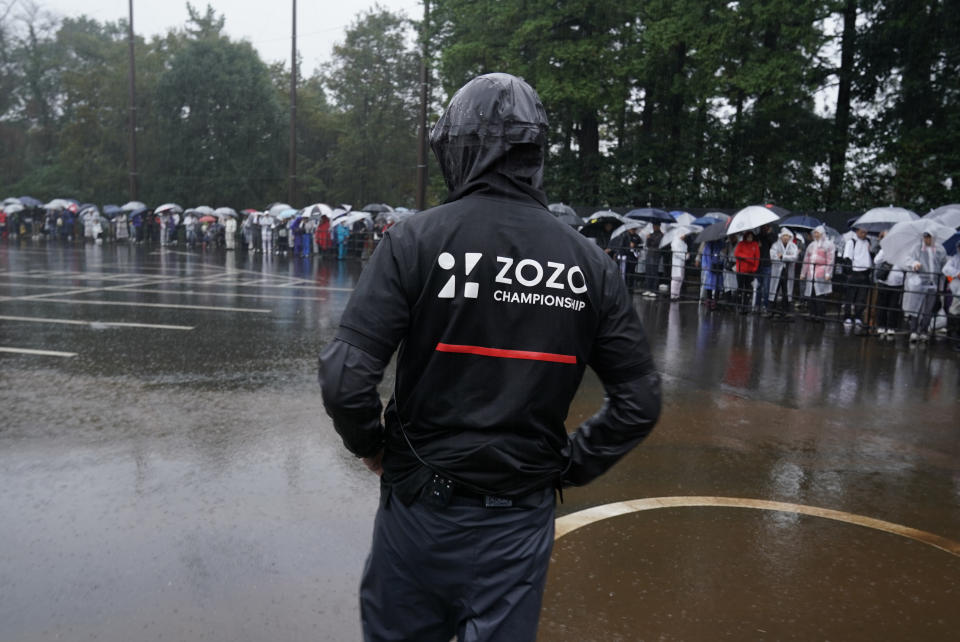 A staff of tournament stands in the rain as spectators wait for shuttle buses at the gate after the second round of the Zozo Championship PGA Tour is postponed due to heavy rain at the Accordia Golf Narashino country club in Inzai, east of Tokyo, Japan, Friday, Oct. 25, 2019. (AP Photo/Lee Jin-man)