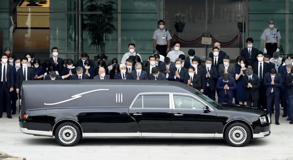 Japanese Prime Minister Fumio Kishida, fourth from right in front, and officials offer prayer as the hearse carrying the body of former Prime Minister Shinzo Abe, makes a brief visit to the Prime Minister's Office after his funeral Tuesday, July 12, 2022, in Tokyo.(Sadayuki Goto/Kyodo News via AP)