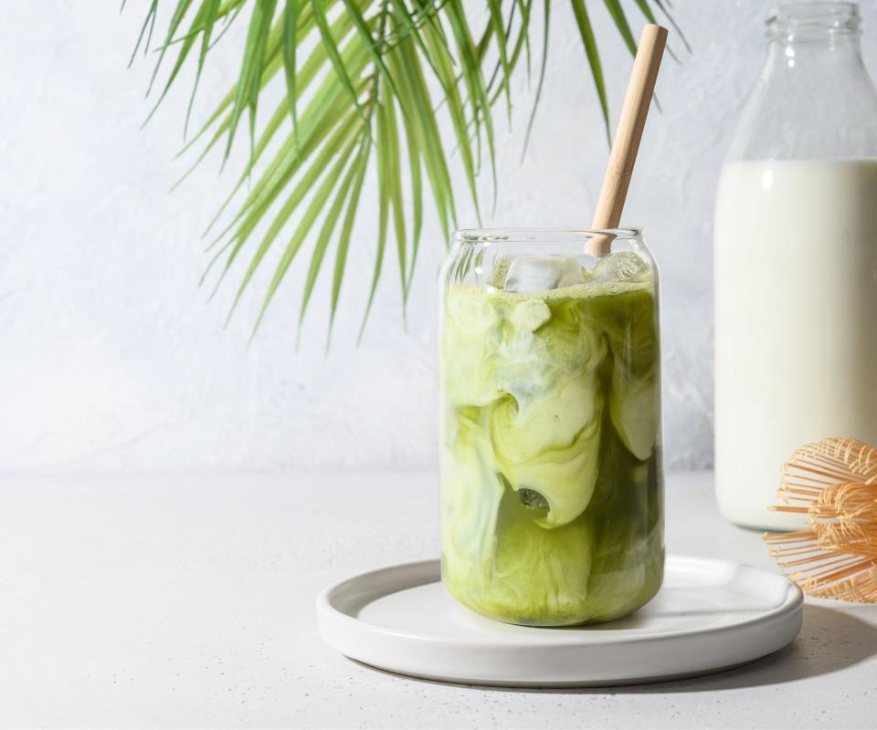 An iced matcha latte on a white countertop with milk and a green leaf behind it